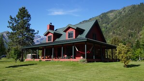 A red house with a green roof, a porch, and a mountain backdrop.