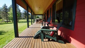A covered wooden deck with outdoor seating, a barbecue grill, and a view of a green lawn.