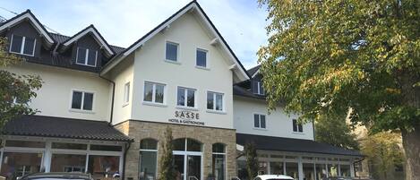 A hotel named SASSE with a modern architectural style, featuring a prominent entrance and a parking area with several cars.