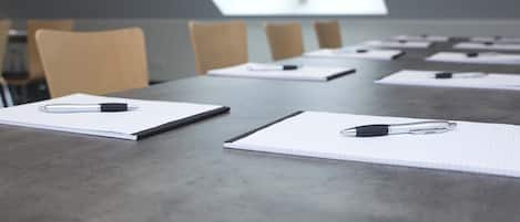 Un salón de conferencias con una larga mesa, varias sillas y cuadernos con bolígrafos encima.