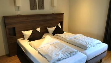 A double bed with white linens and two pillows, a wooden headboard, and two wall-mounted lamps.