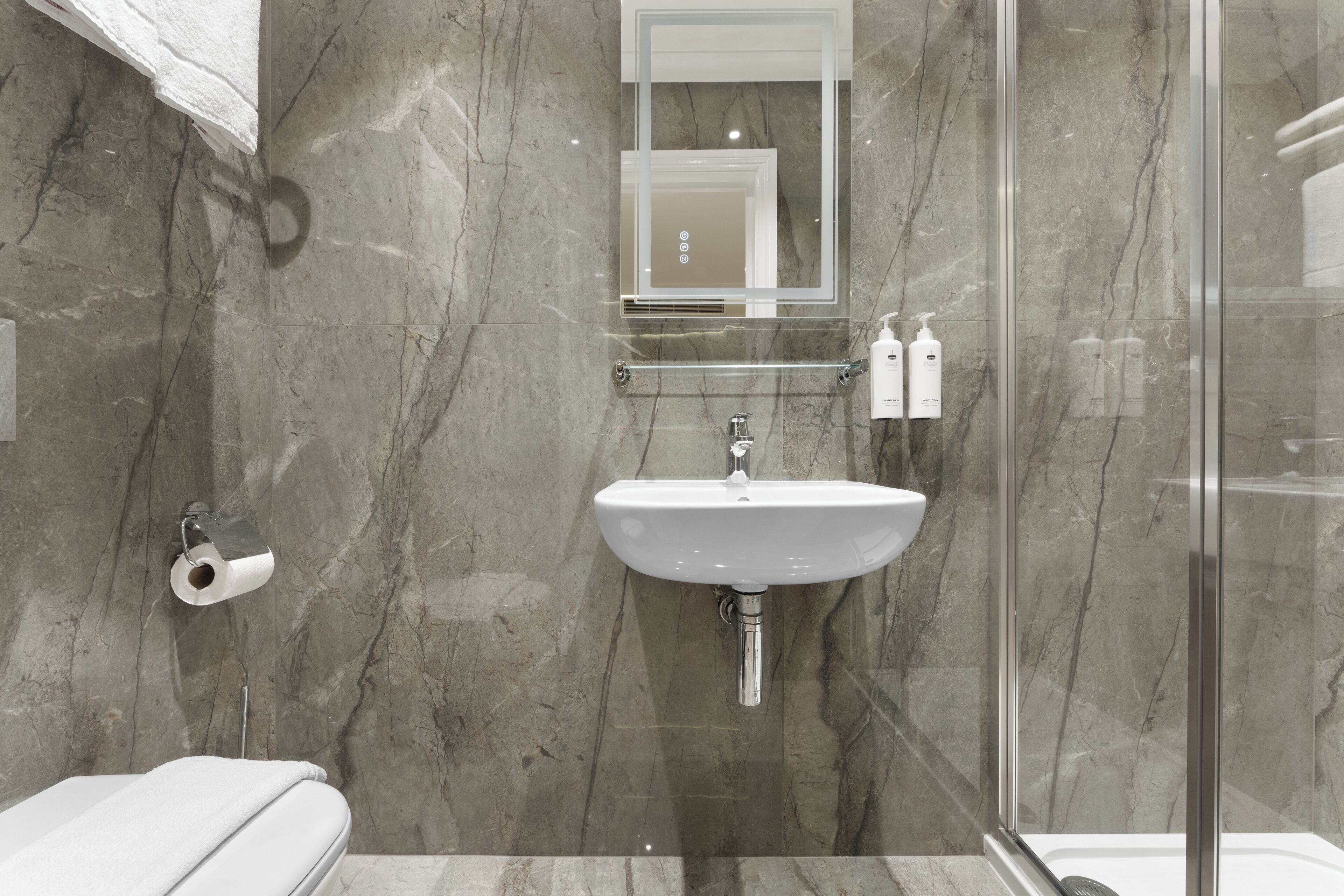 Une salle de bain moderne avec un mur en marbre, une cabine de douche en verre, un lavabo et un porte-rouleau de papier toilette.