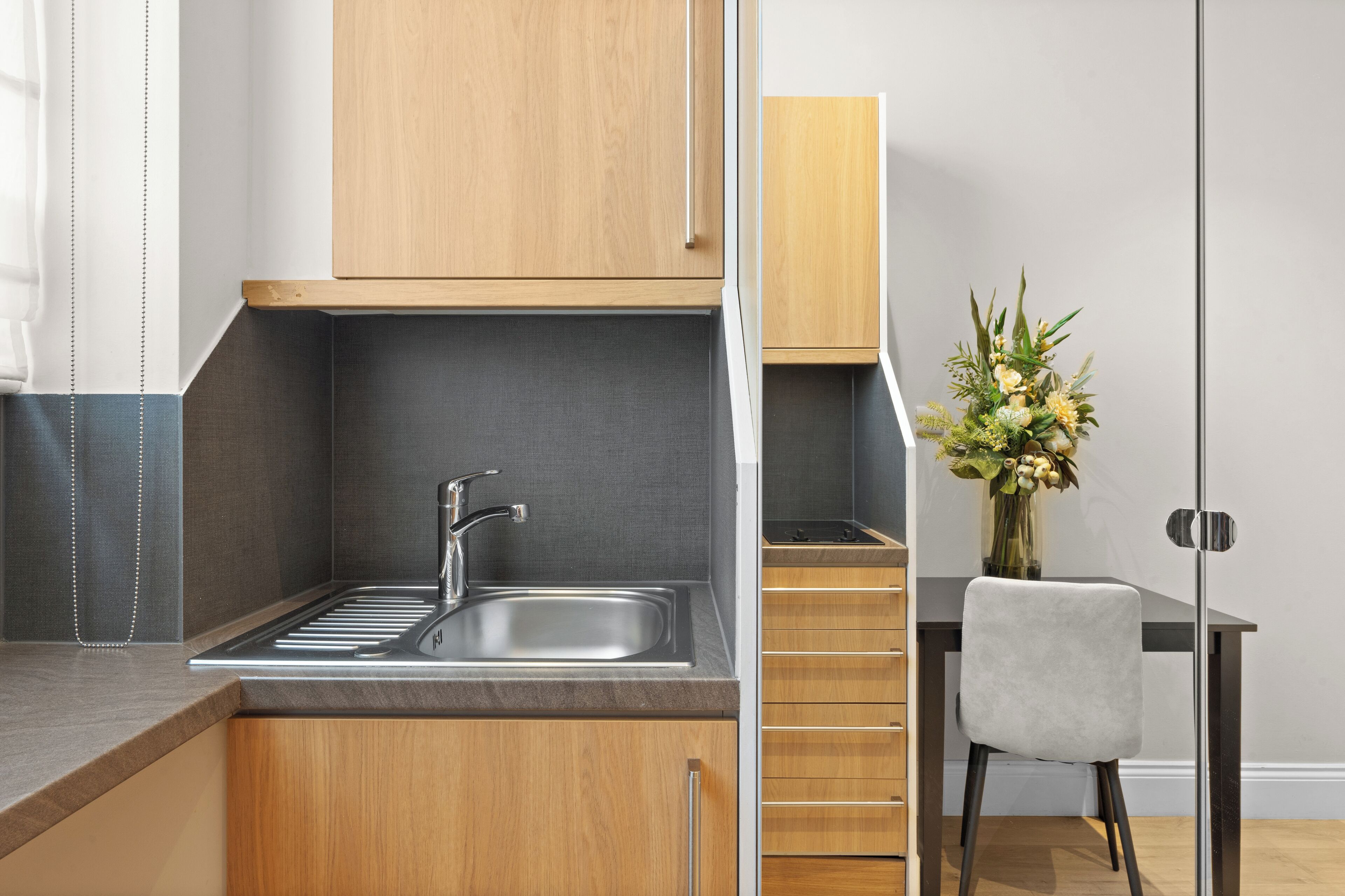Una cocina moderna con un lavamanos de acero inoxidable, armarios de madera y una encimera negra.