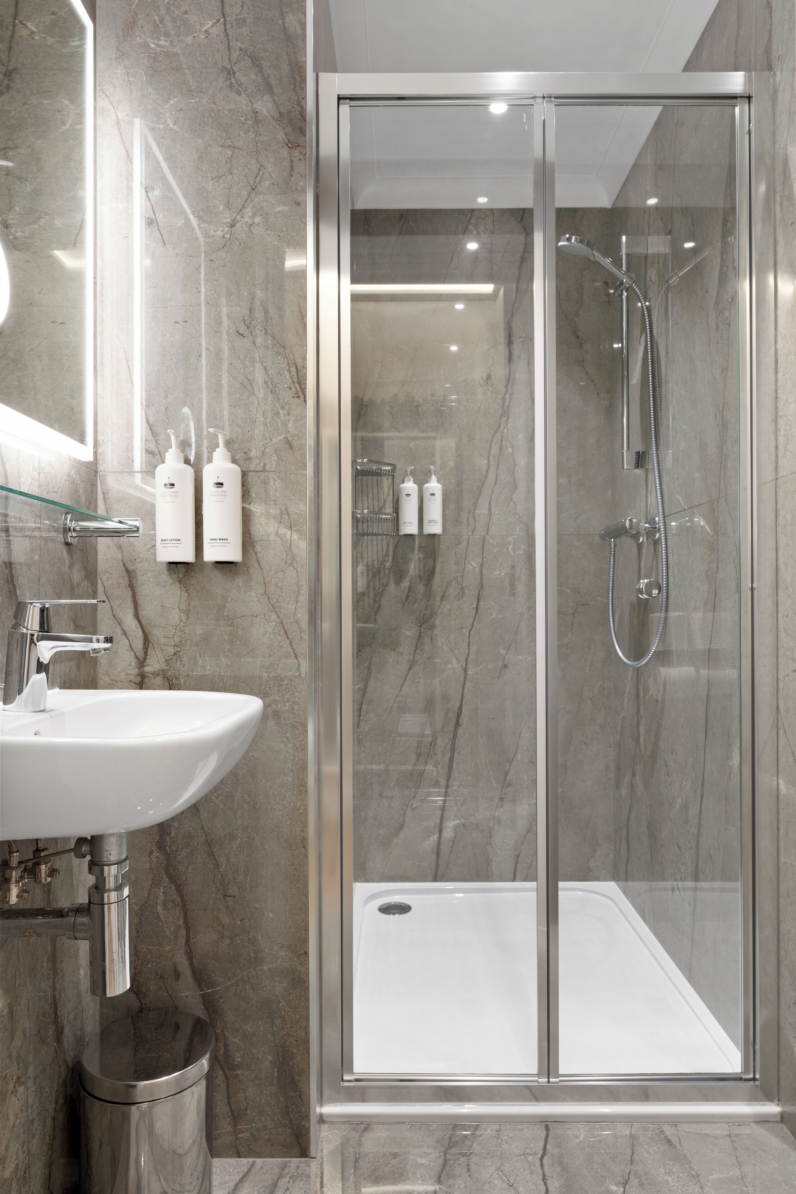 Een moderne badkamer met een douchecabine van glas, een wit wastafelmeubel en marmeren wanden.