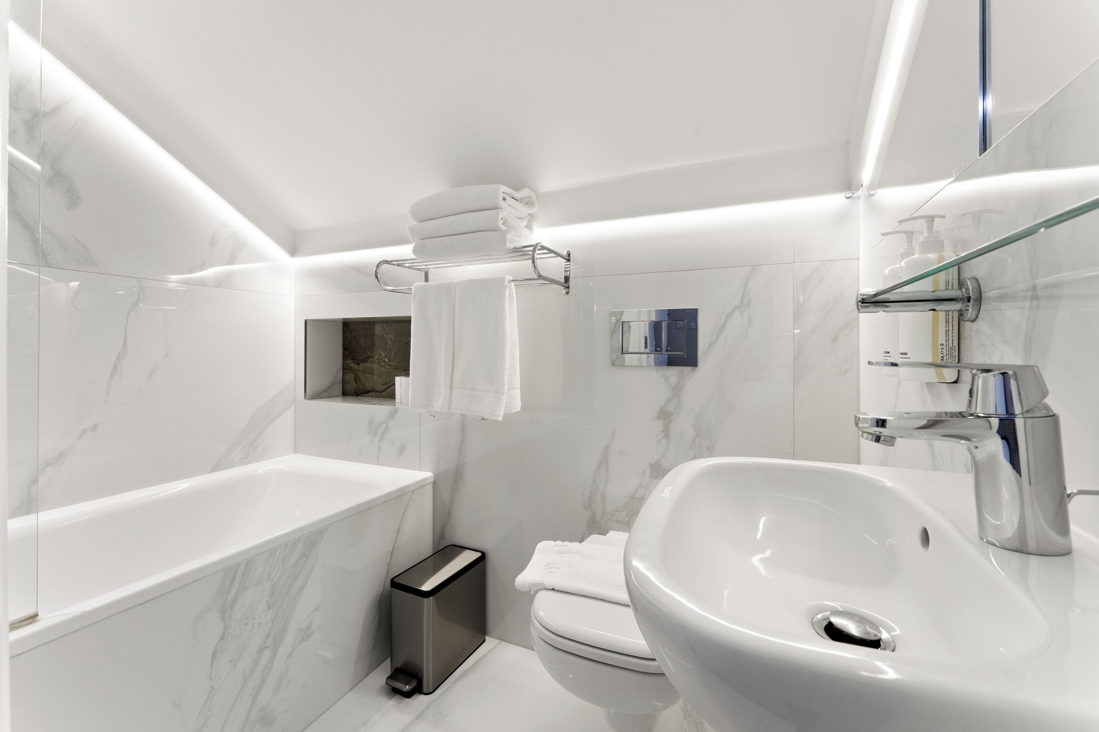A modern bathroom with a white sink, a glass-enclosed shower, and a marble-tiled wall.