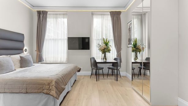 A modern bedroom with a large bed, a desk with chairs, and a TV mounted on the wall. - Cleveland Residences Russell Square (London)
