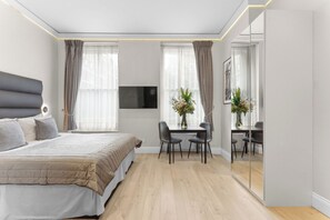 A modern bedroom with a large bed, a desk with chairs, and a TV mounted on the wall. - Cleveland Residences Russell Square (London)