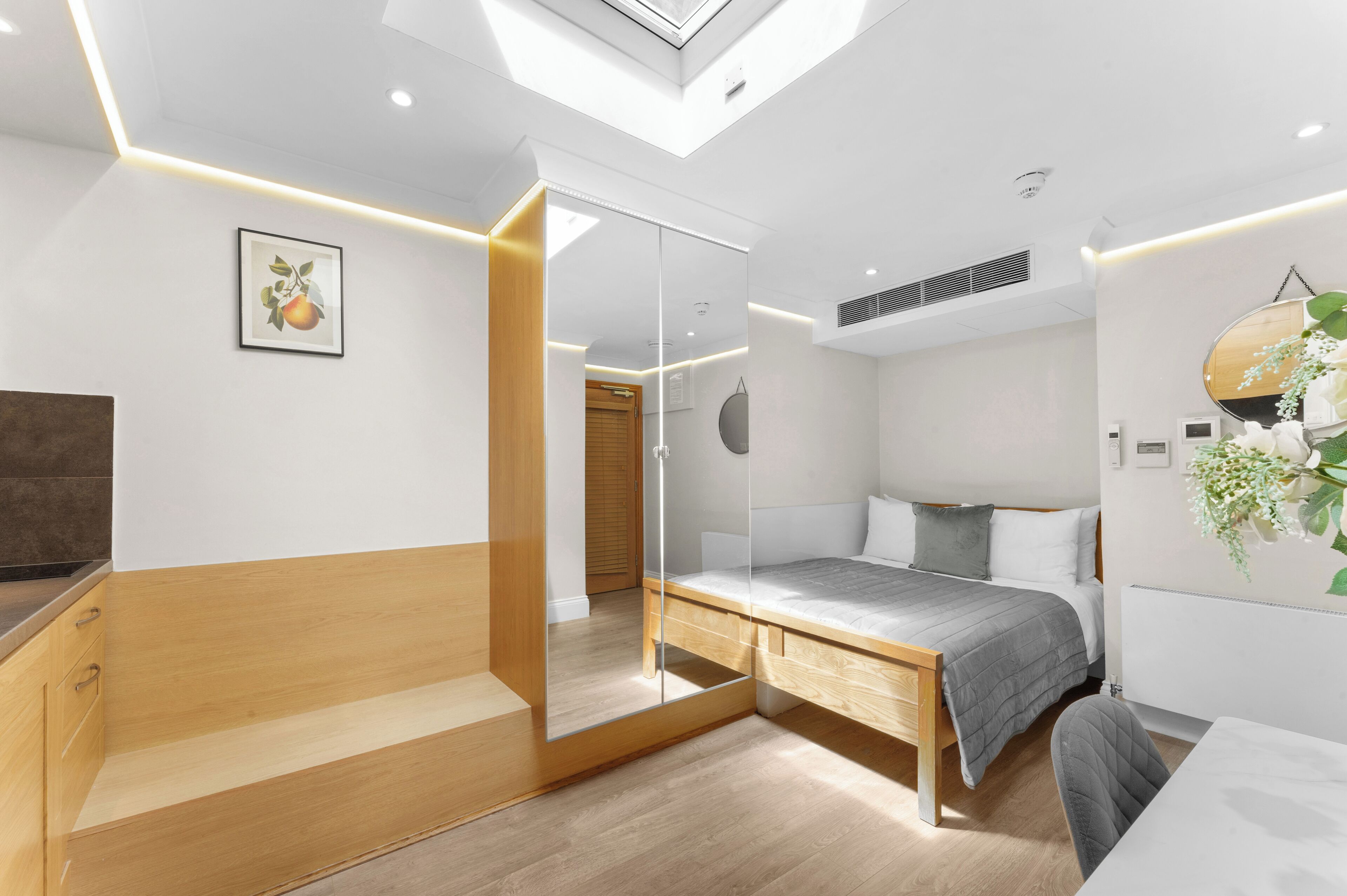 Ein modernes Schlafzimmer mit Dachfenster, einem Bett mit grauer Tagesdecke, einer Holzbank und einem Spiegel.