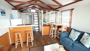 Un espace de vie compact comprenant un coin cuisine, un coin repas et un espace détente avec un canapé et des tabourets de bar.