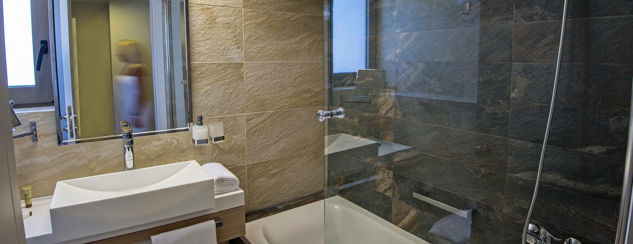 Une salle de bain moderne avec un grand miroir, un lavabo blanc, une baignoire et une douche à l’italienne.