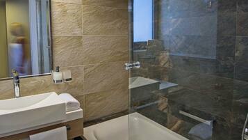 Une salle de bain moderne avec un grand miroir, un lavabo blanc, une baignoire et une douche à l’italienne.