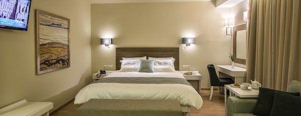 A hotel room with a bed, bedside tables, a desk with a chair, a television, and a painting on the wall. - Swell Boutique Hotel (Rethymno)