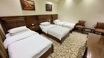 A hotel room with four beds, two nightstands, a wooden headboard, a patterned carpet, and two framed pictures on the wall.