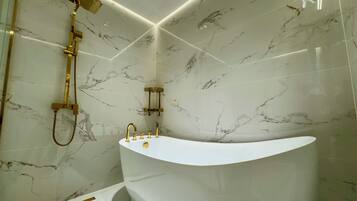 A modern bathroom with a freestanding bathtub, a gold showerhead, and marble walls.