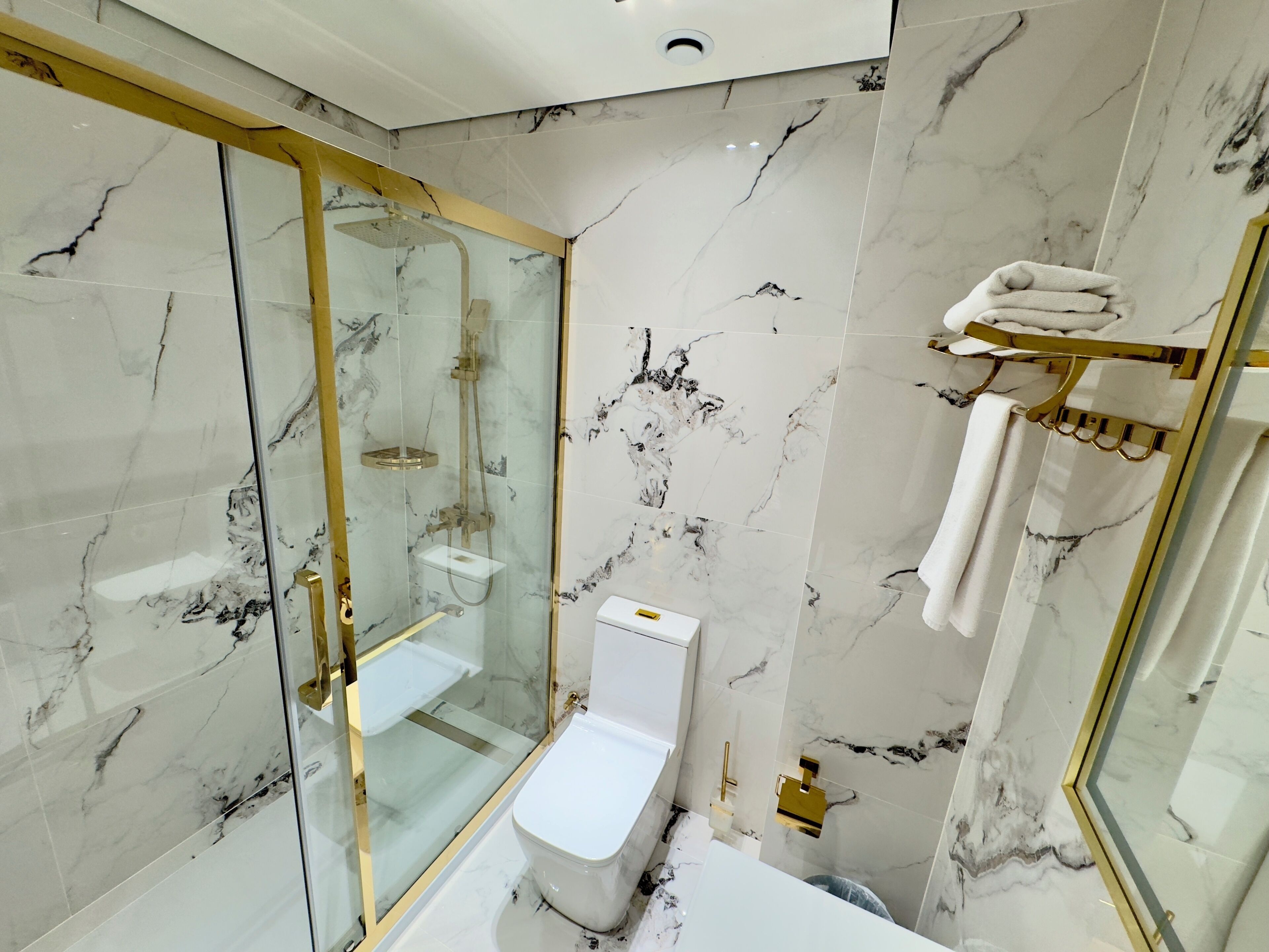 Et moderne badeværelse med en glasafskærmet brusekabine, et hvidt toilet og marmorvægge.