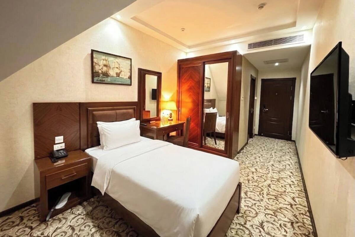 A hotel room with a bed, bedside table, lamp, mirror, wardrobe, and a television.