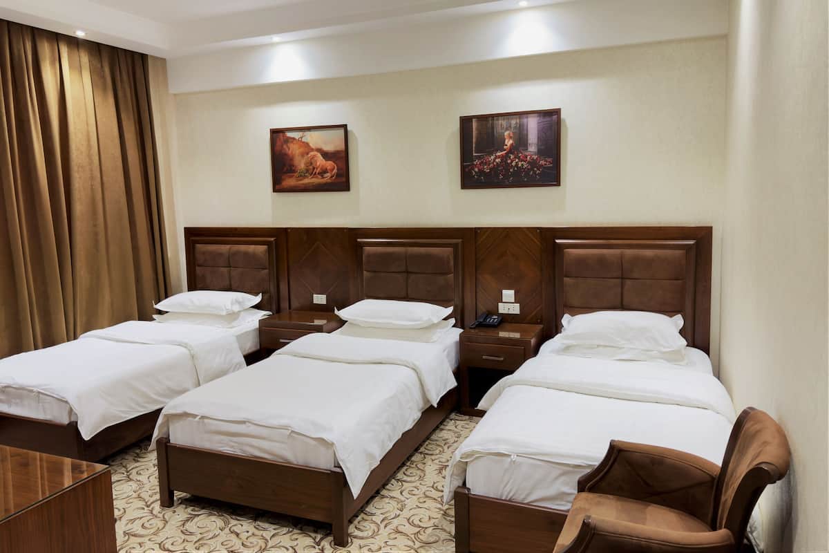 A hotel room with three single beds, wooden headboards, white bedding, and a patterned carpet.