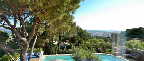 A pool area with a view of the city, surrounded by trees and a clear sky.