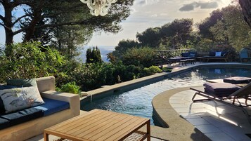 Zona junto a la piscina con sofá, sillones de descanso y vista al mar.