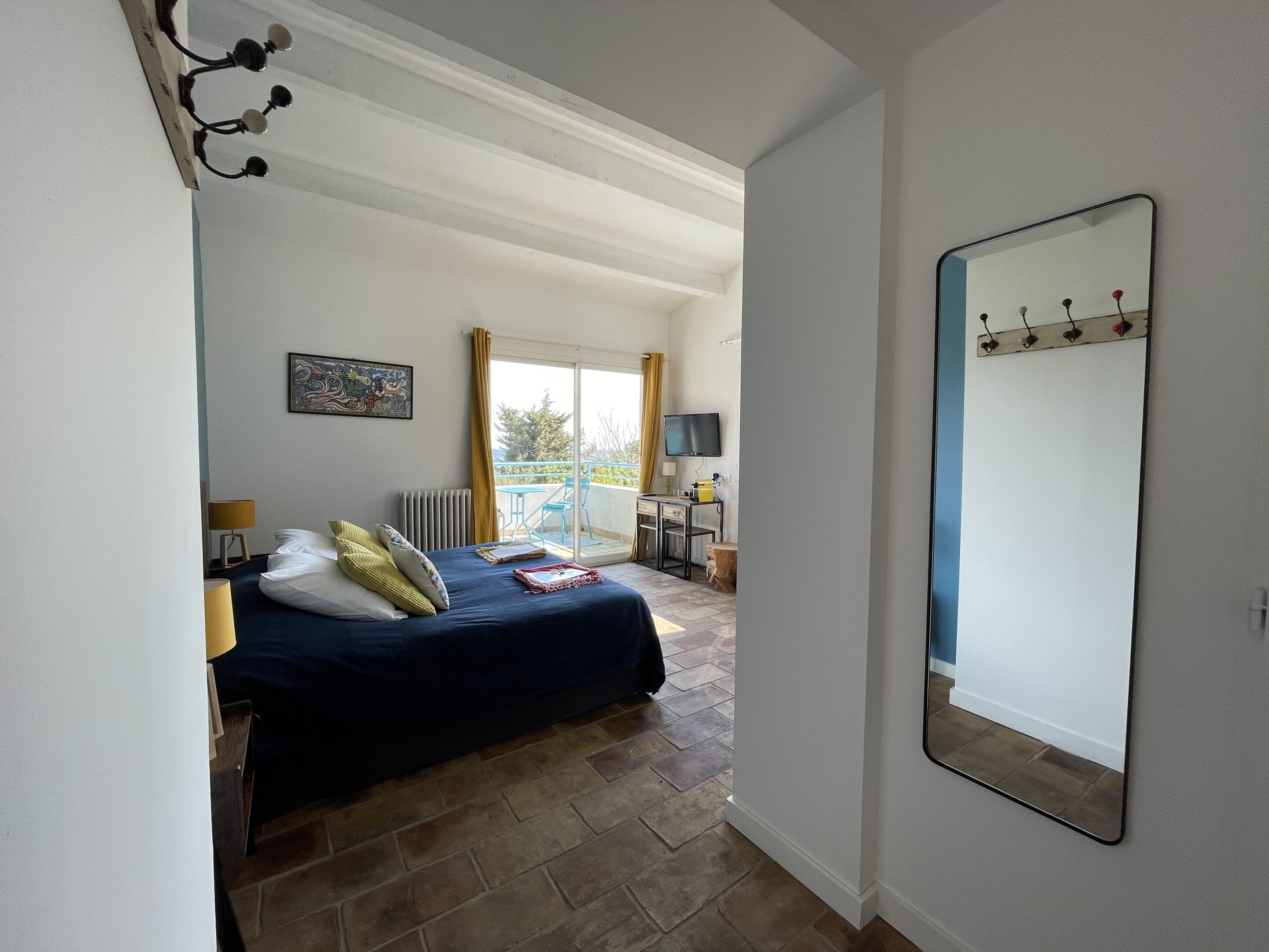 A bedroom with a bed, a desk, a chair, a TV, and a balcony with a view.