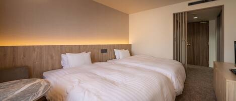 A hotel room with a large bed, a desk, and a chair. There is a wooden headboard and a wall-mounted lamp.