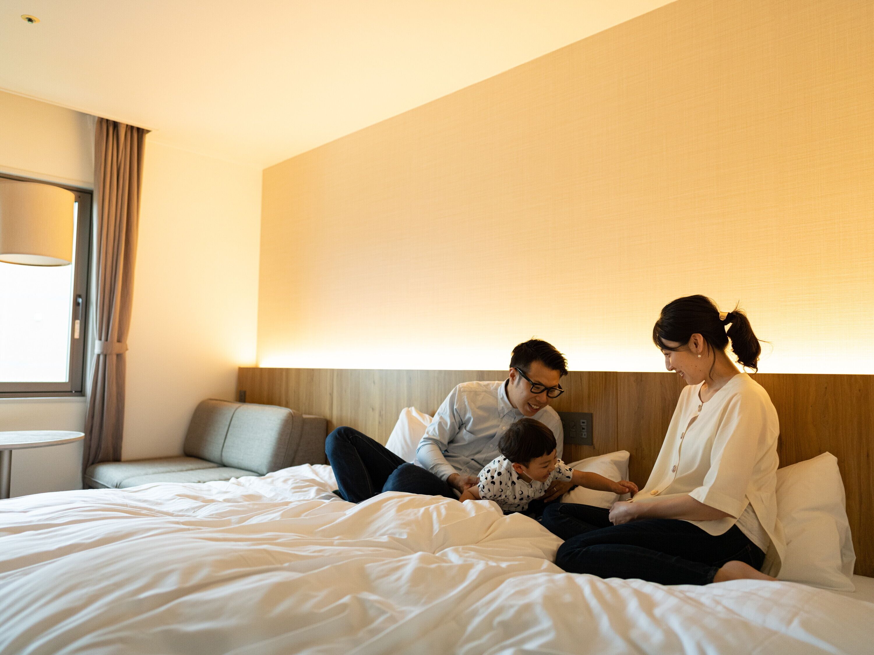 Habitación de hotel con cama, mesita de noche, lámpara y ventana con cortinas.