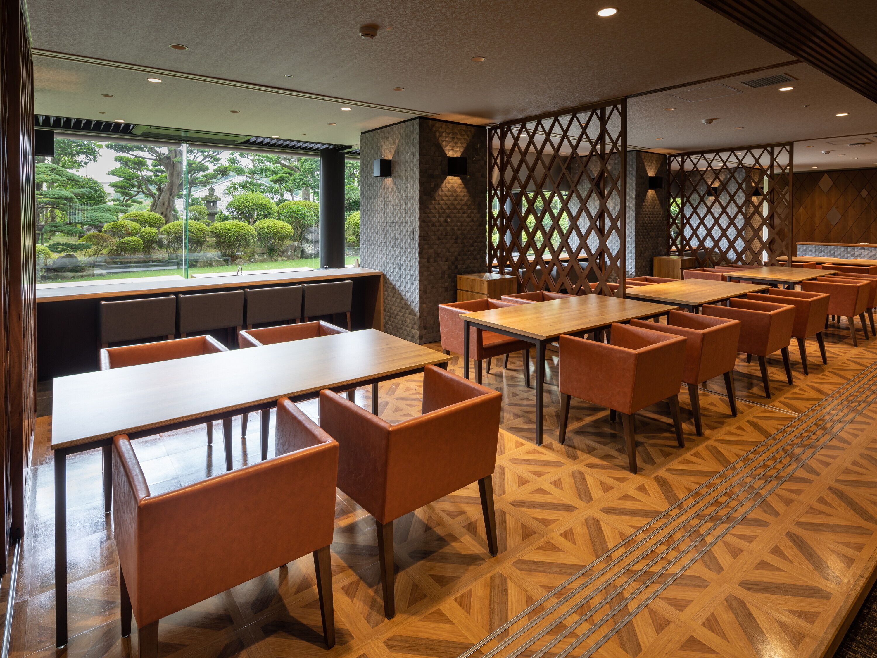A restaurant with wooden tables and chairs, a patterned floor, and a view of greenery outside.