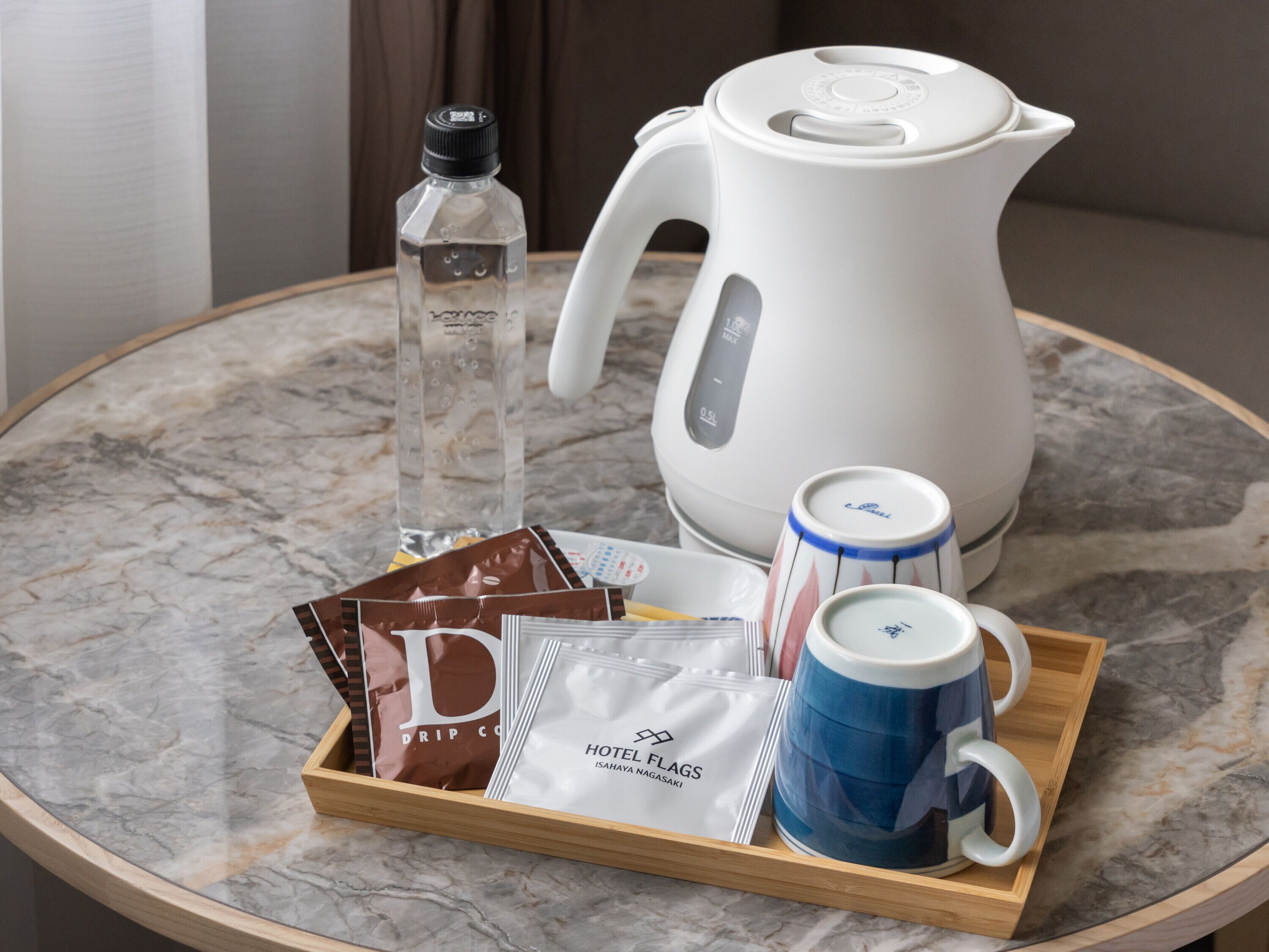 A tray with a coffee maker, a bottle of water, a mug, and some packaged food items on a marble table.