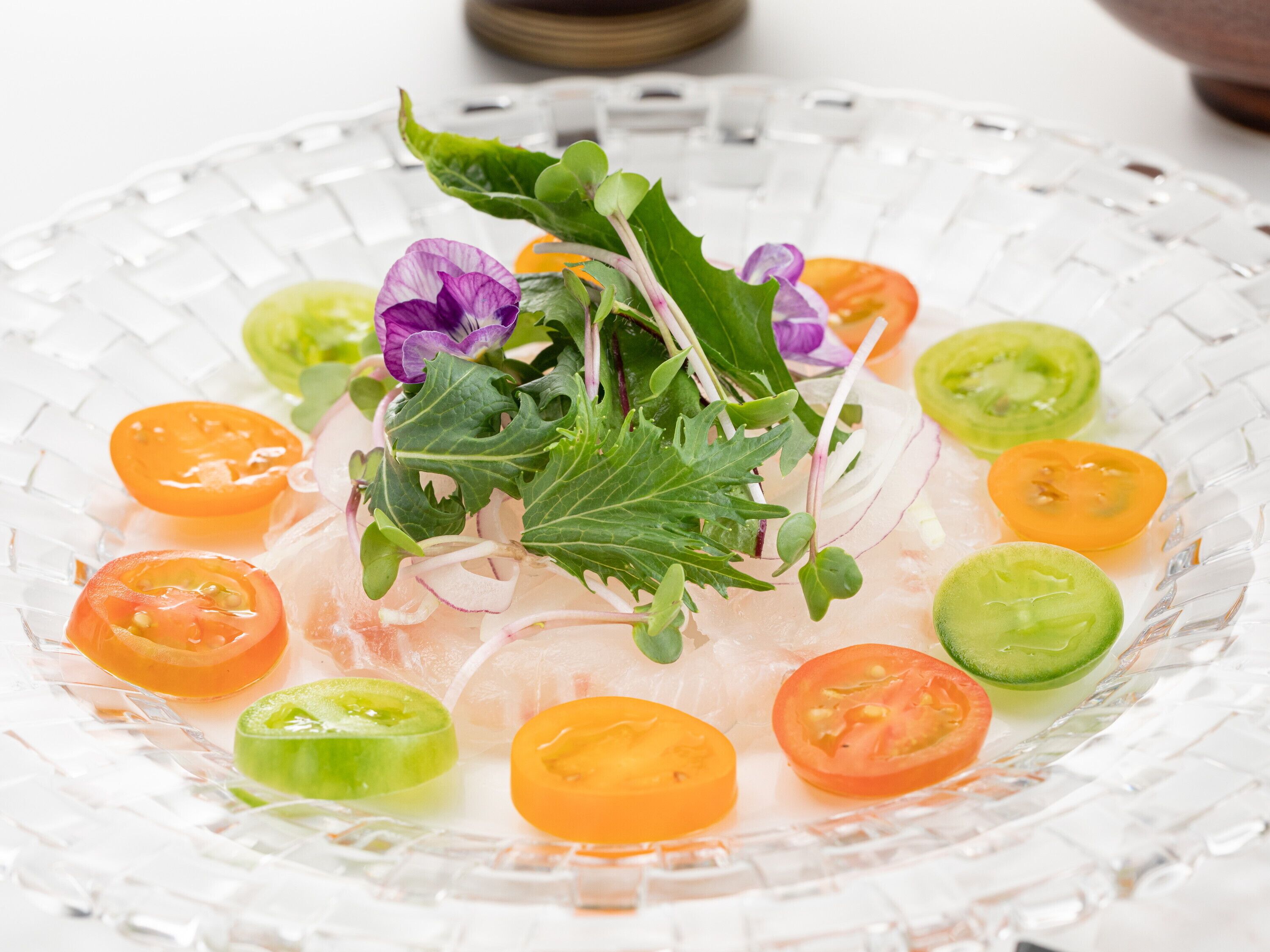 Una fuente de vidrio con una ensalada de diversas verduras y hojas verdes.