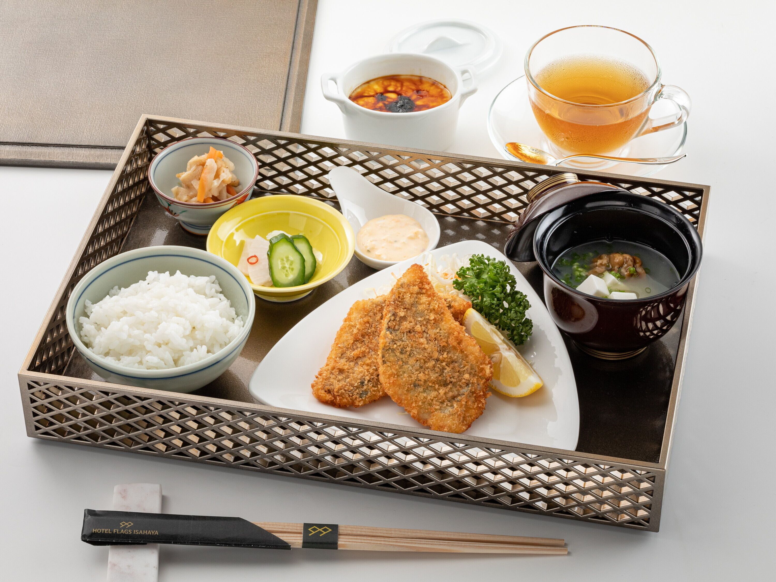 Una bandeja con diversos platos japoneses, incluyendo arroz, tempura y sopa, junto con palillos y una taza de té.