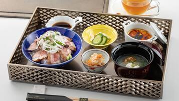 A tray with various Japanese dishes, including a bowl of rice topped with meat and vegetables, a bowl of soup, and a cup of tea.