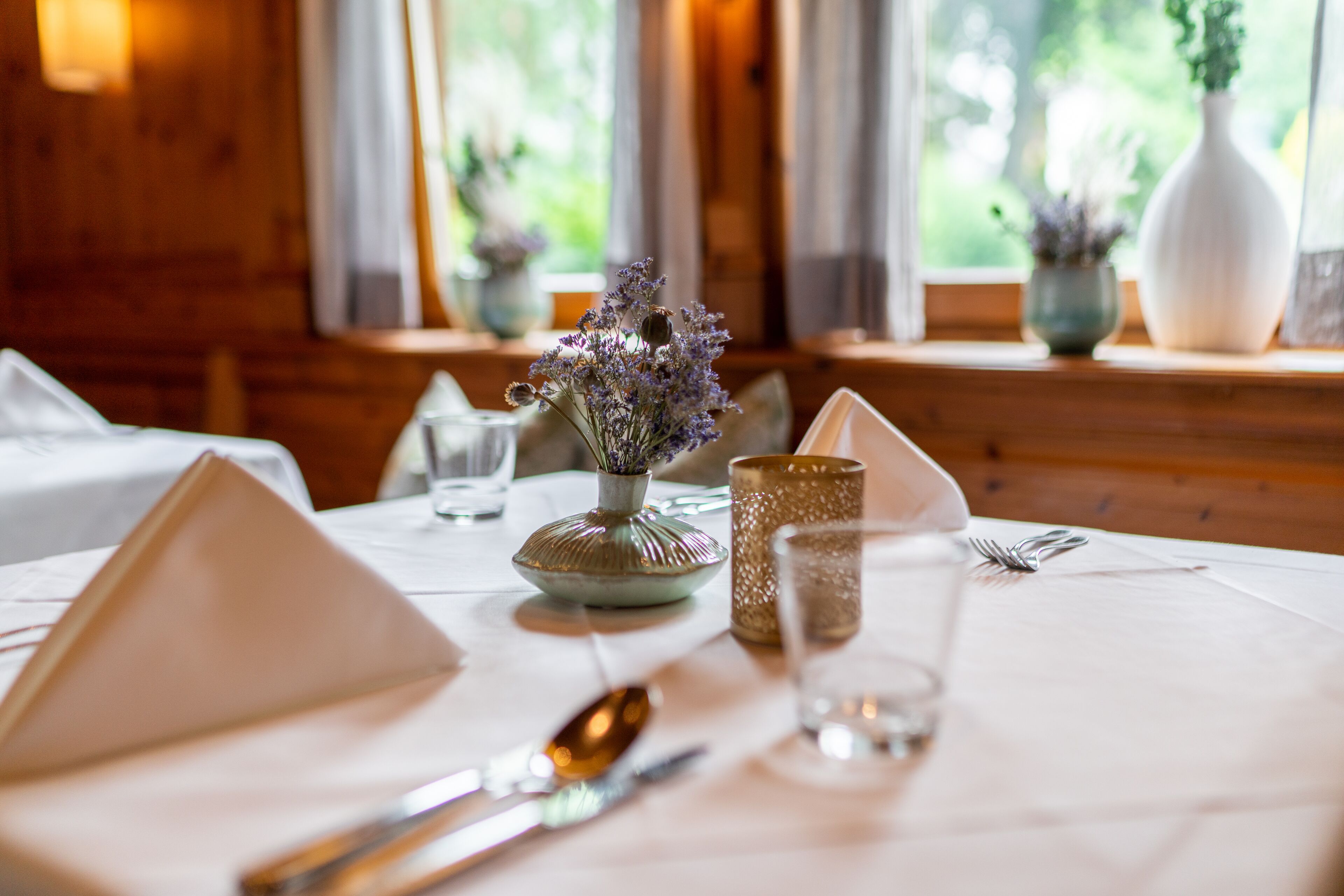 Una mesa de comedor dispuesta con una servilleta con forma de pirámide, una cuchara, un tenedor, un vaso y un florero con flores.