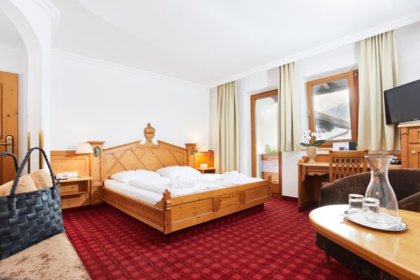 Habitación de hotel con una cama de madera, un escritorio con silla, un televisor y una alfombra roja a cuadros.