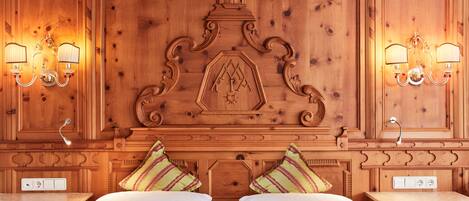 A double bed with two pillows, a wooden headboard with a decorative crest, and two wall-mounted lamps.