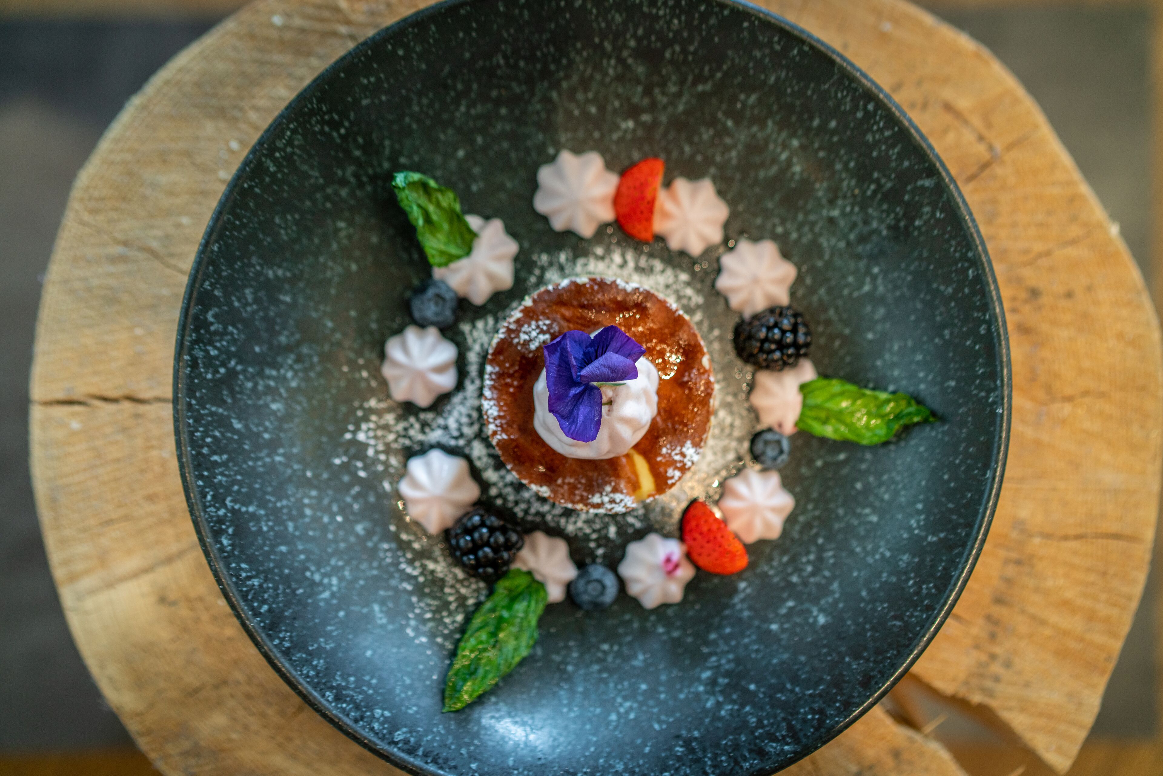 Dessert auf einem schwarzen Teller mit verschiedenen Früchten und einer Blüte.