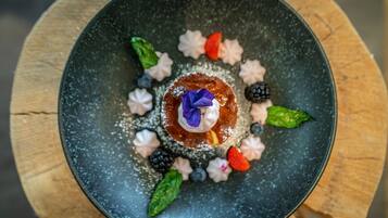Dessert auf einem schwarzen Teller mit verschiedenen Früchten und einer Blüte.