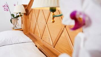Una cama bien hecha con sábanas blancas, cabecera de madera, mesita de noche con lámpara y un jarrón con flores.