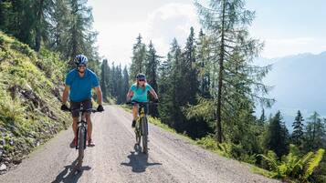 Two people riding bicycles on a gravel road surrounded by trees and mountains.
