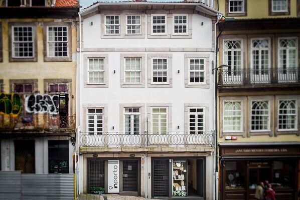 Un edificio de varios pisos con fachada blanca, múltiples ventanas y un escaparate con un letrero.