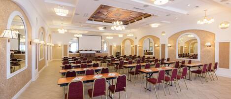 Un salón de conferencias con varias mesas y sillas, arcos y candelabros.