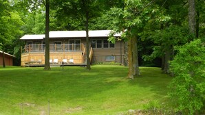 A house with a deck, a grassy yard, and a dock extending into a body of water.