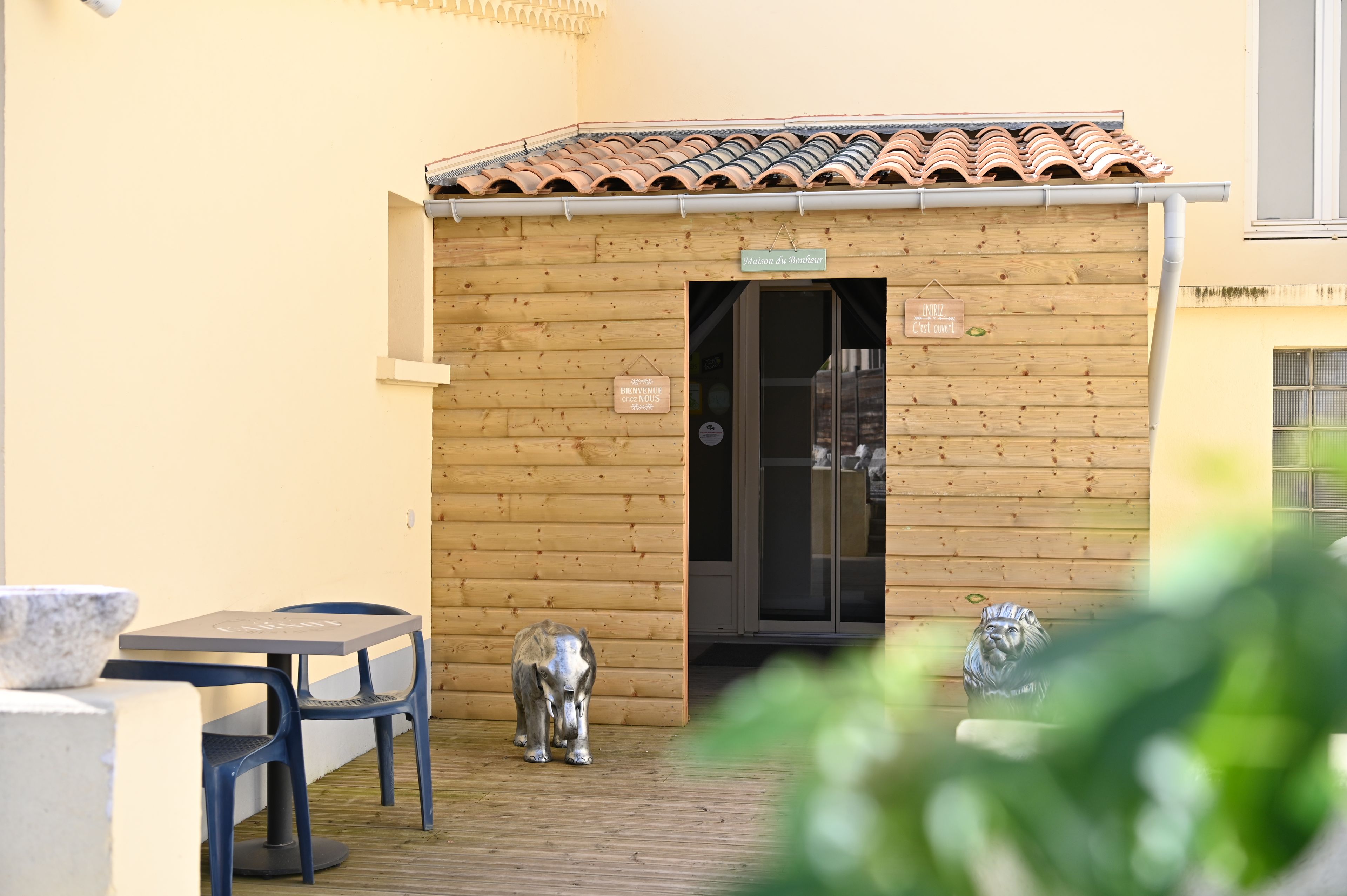 A wooden exterior wall with a tiled roof, a wooden door, and a small outdoor seating area with a table and chairs.