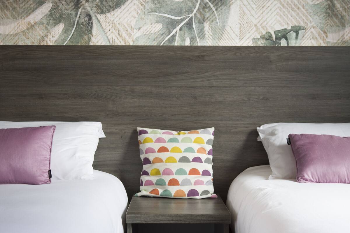 A hotel room with two beds, a nightstand, and a wall with a leaf pattern.