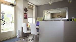 Un área de recepción con un mostrador, sillas, un espejo grande y una puerta que da a vistas del exterior.