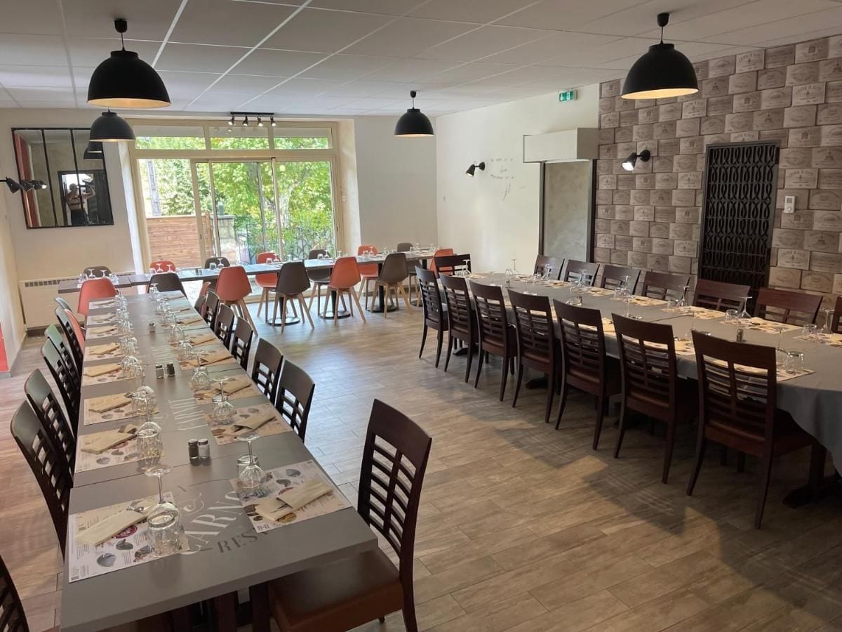 A long dining table with chairs, overhead lighting, and a brick wall with plaques.
