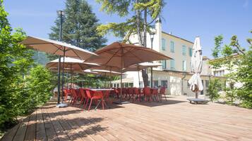 An outdoor patio with wooden flooring, red chairs, and large umbrellas providing shade.