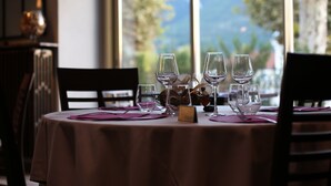Una mesa preparada para una comida, con copas de vino, un cuenco pequeño y una carta, con vistas a la vegetación y montañas a través de la ventana.
