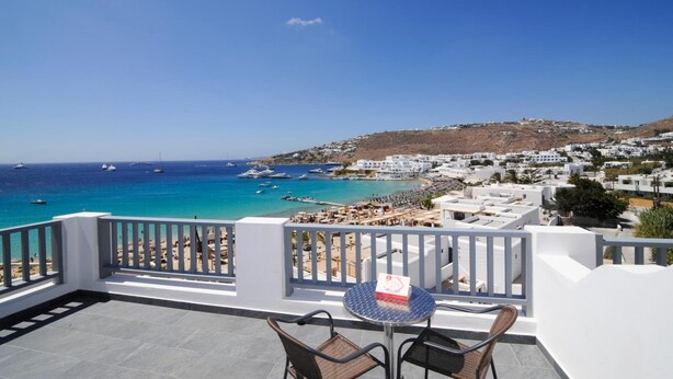 A balcony with a view of a beach and boats, white buildings, and a clear sky. - Hotel Anna (Mykonos)