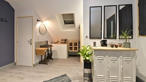 A modern kitchen with a wooden countertop, a coffee machine, and a potted plant. There is a small window above the sink and a cabinet with a mirror above it.