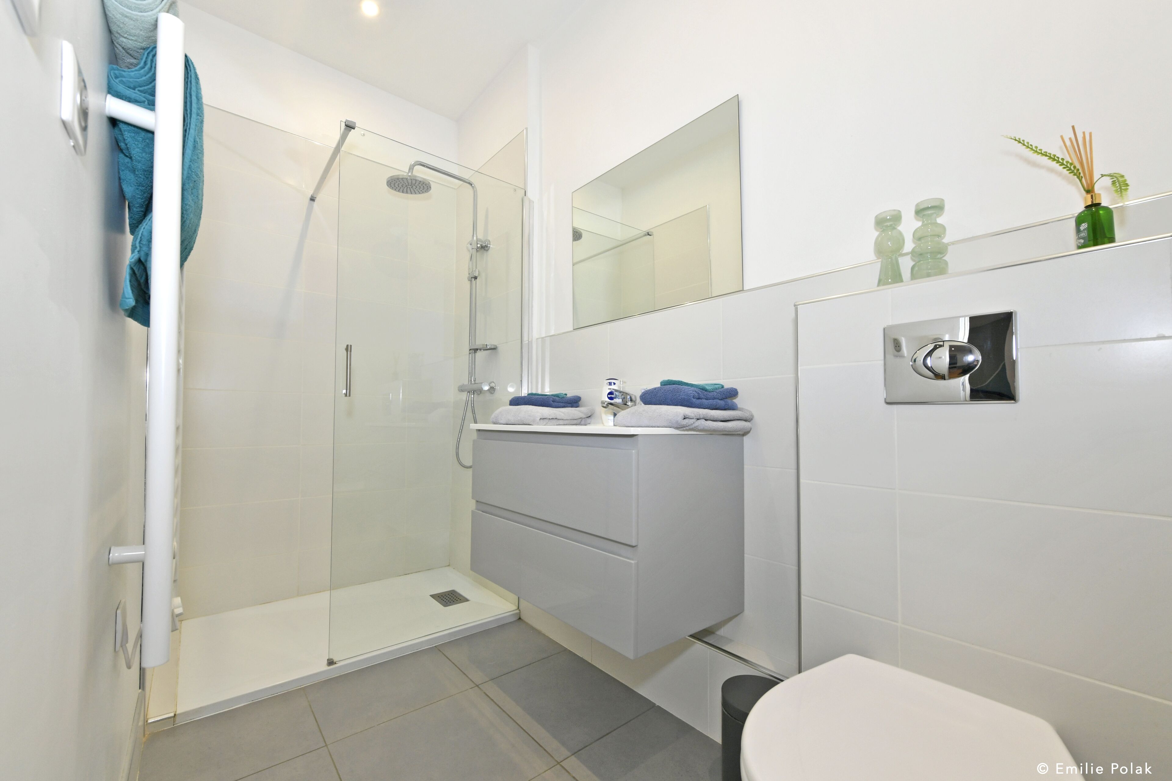 A modern bathroom with a glass shower enclosure, a white sink with a mirror above, and a toilet.